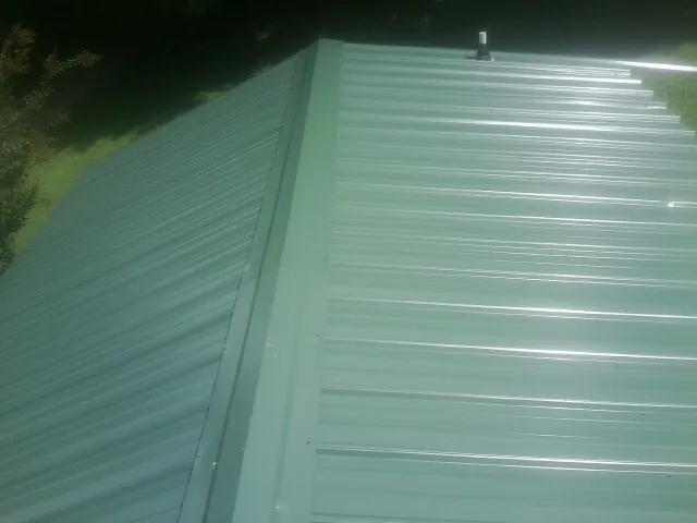 New green metal panels meeting at the ridge of a roof — Flat Roof Repair work by our crew in Benton