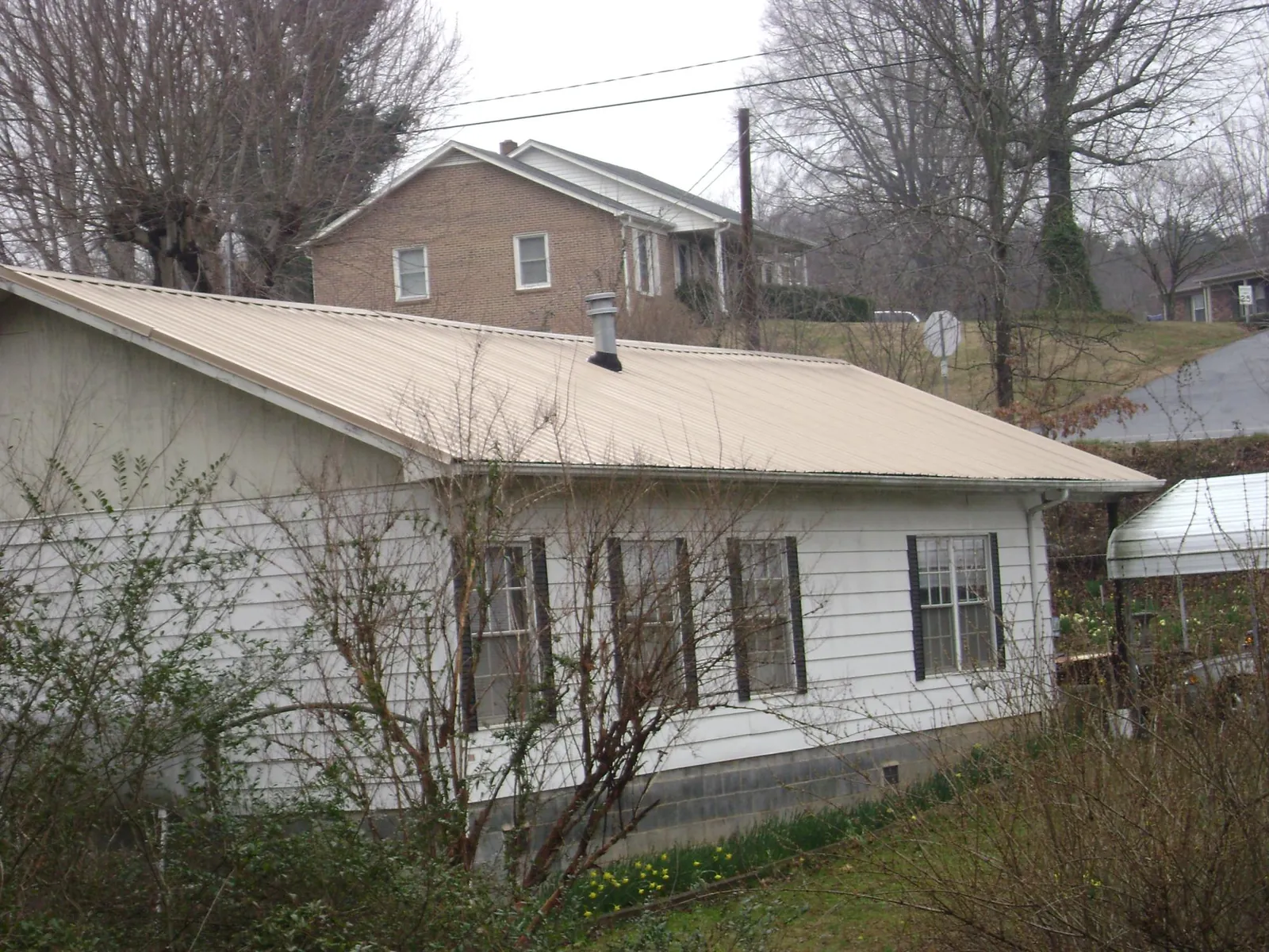 Tan metal roof on a white sided house set into a hillside — Commercial Roofing by Roofing Brothers in Benton
